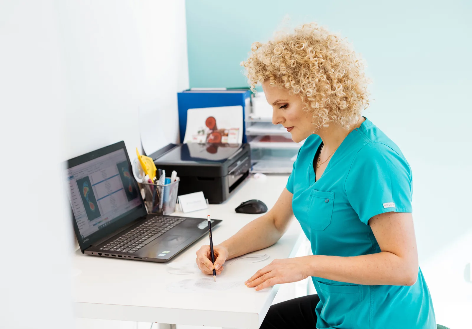Stanowisko diagnostyki FootMedica: fizjoterapeutka przy komputerze z wynikiem badania